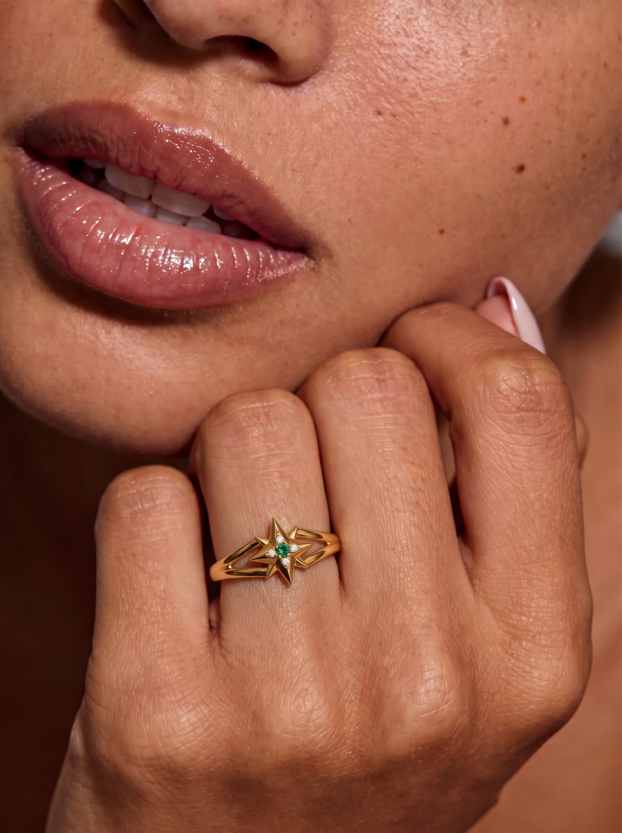 A close-up of a person's hand resting near their chin, wearing a delicate gold ring with a small diamond stones on the sides.