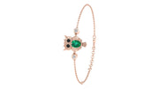 A delicate rose gold chain bracelet featuring an owl charm with a green emerald center, black and white eyes, and small clear accent stones, shown on a plain white background.