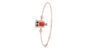 A delicate rose gold chain bracelet featuring a central owl charm with a red coral gemstone, black eyes, and small clear stones, shown on a plain white background.