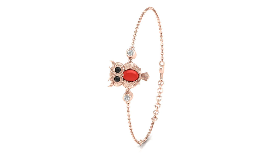 A delicate rose gold chain bracelet featuring a central owl charm with a red coral gemstone, black eyes, and small clear stones, shown on a plain white background.