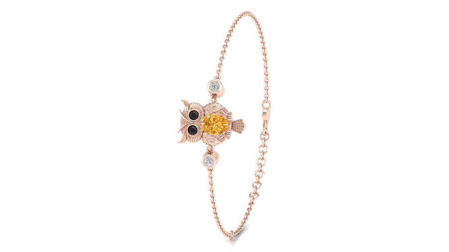 A delicate rose gold chain bracelet featuring a central owl charm with a yellow sapphire centrepiece, black eyes, and small clear stones, shown on a plain white background.