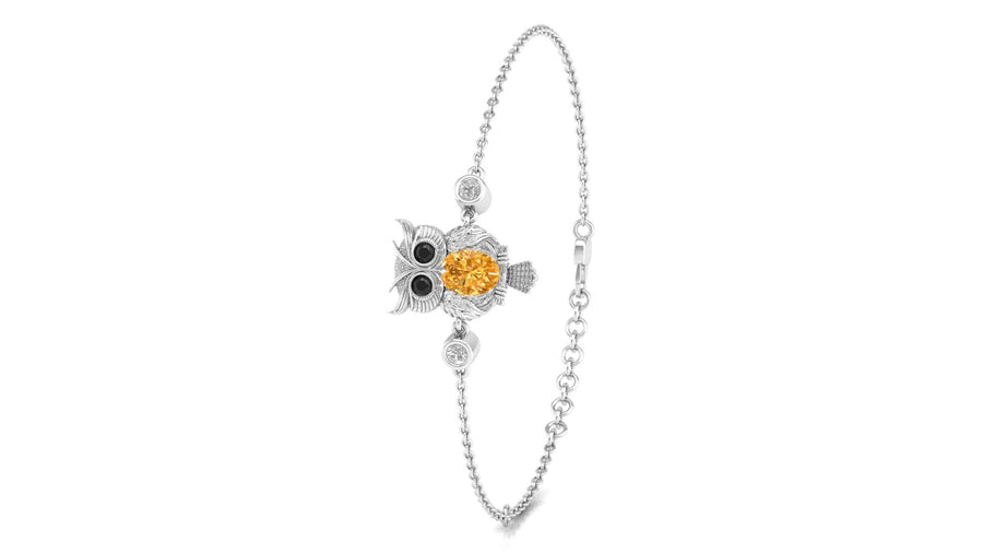 A White gold ball chain bracelet featuring an owl charm with a prominent round yellow Sapphire gemstone on its chest, set against a plain white background.