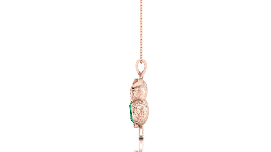 A rose gold pendant shaped like a sleeping owl, featuring a textured finish and a small green emerald centrestone on its wing, hanging from a delicate rose gold chain against a white background.