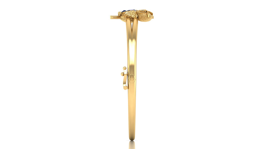 A gold bangle bracelet with a decorative snake head clasp and a small blue sapphire gemstone, shown from the side on a white background.