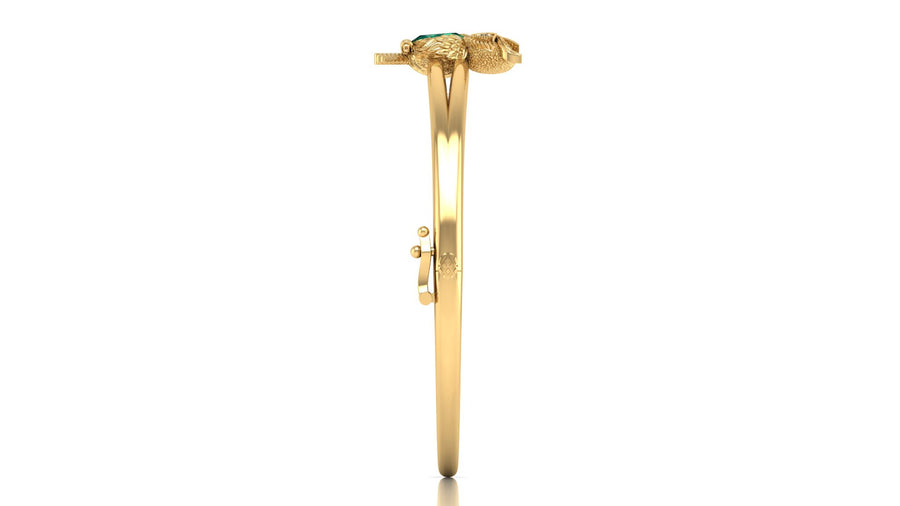A gold bangle bracelet with a decorative snake head clasp and a small green stone, shown from the side on a white background.