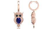 Rose gold owl-shaped earrings with blue sapphire gemstones on a white background