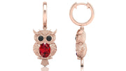 Rose gold owl-shaped earrings with ruby gemstones on a white background