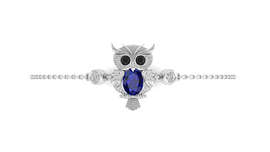 A white gold owl pendant bracelet featuring a central oval blue sapphire gemstone, black eyes, and small clear accent stones, shown on a plain white background.