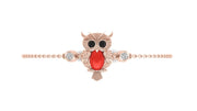 A rose gold owl charm bracelet with a red coral, black eyes, and clear gemstone accents, shown on a plain white background.
