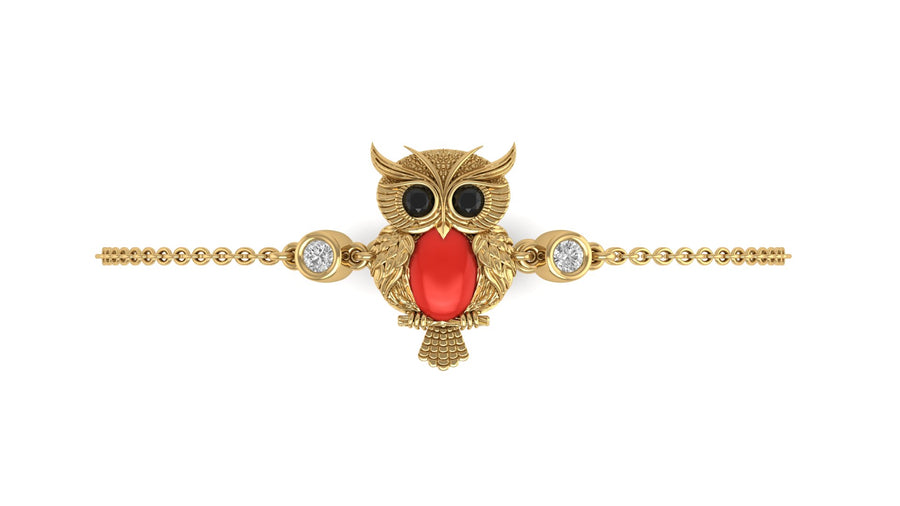 A gold owl pendant bracelet featuring a large red coral-cut center stone, black stone eyes, and small clear accent stones on either side, set on a delicate gold chain against a plain white background.