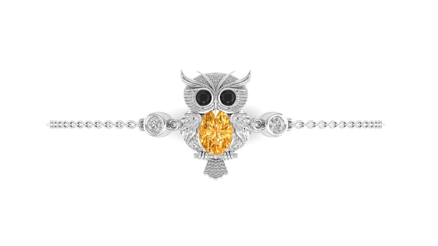 An owl-shaped pendant bracelet in silver-toned metal with a large oval yellow sapphire center stone and small dark eye accents, shown on a plain white background.