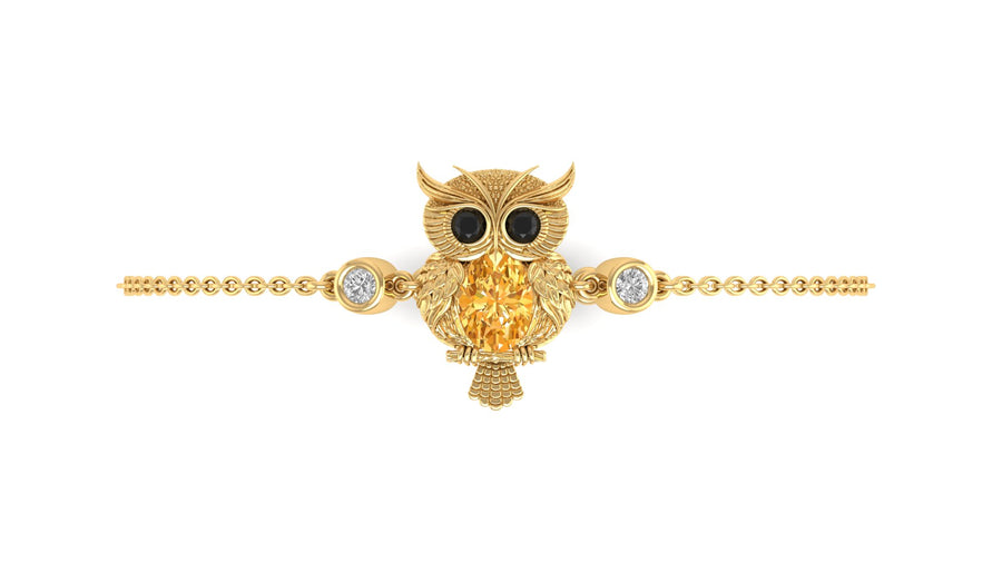 A gold owl pendant bracelet featuring a large Yellow sapphire center stone, black stone eyes, and small clear accent stones on either side, set on a delicate gold chain against a plain white background.