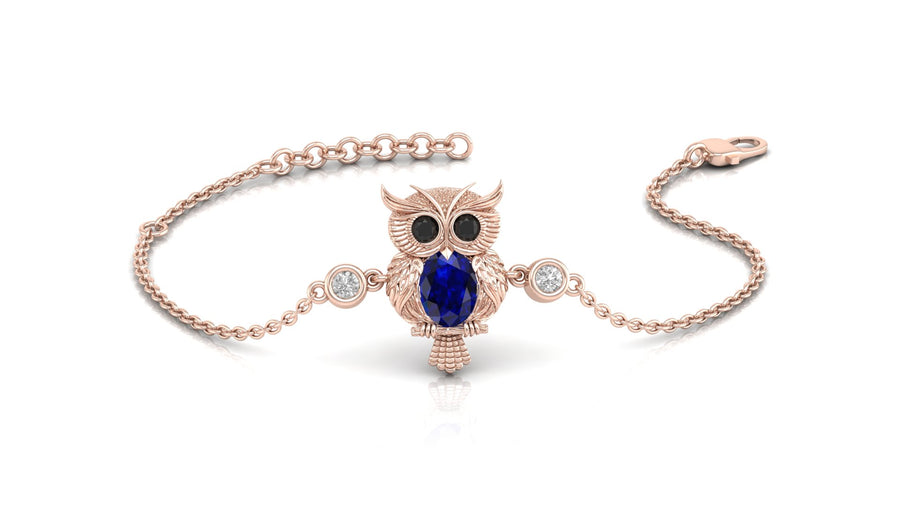 A delicate rose gold chain bracelet featuring an owl pendant with a large blue sapphire gemstone and small clear accent stones, displayed on a clean white background.