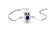 A white gold chain bracelet featuring an owl pendant with a deep blue sapphire oval gemstone and small clear accent stones, shown on a clean white background.