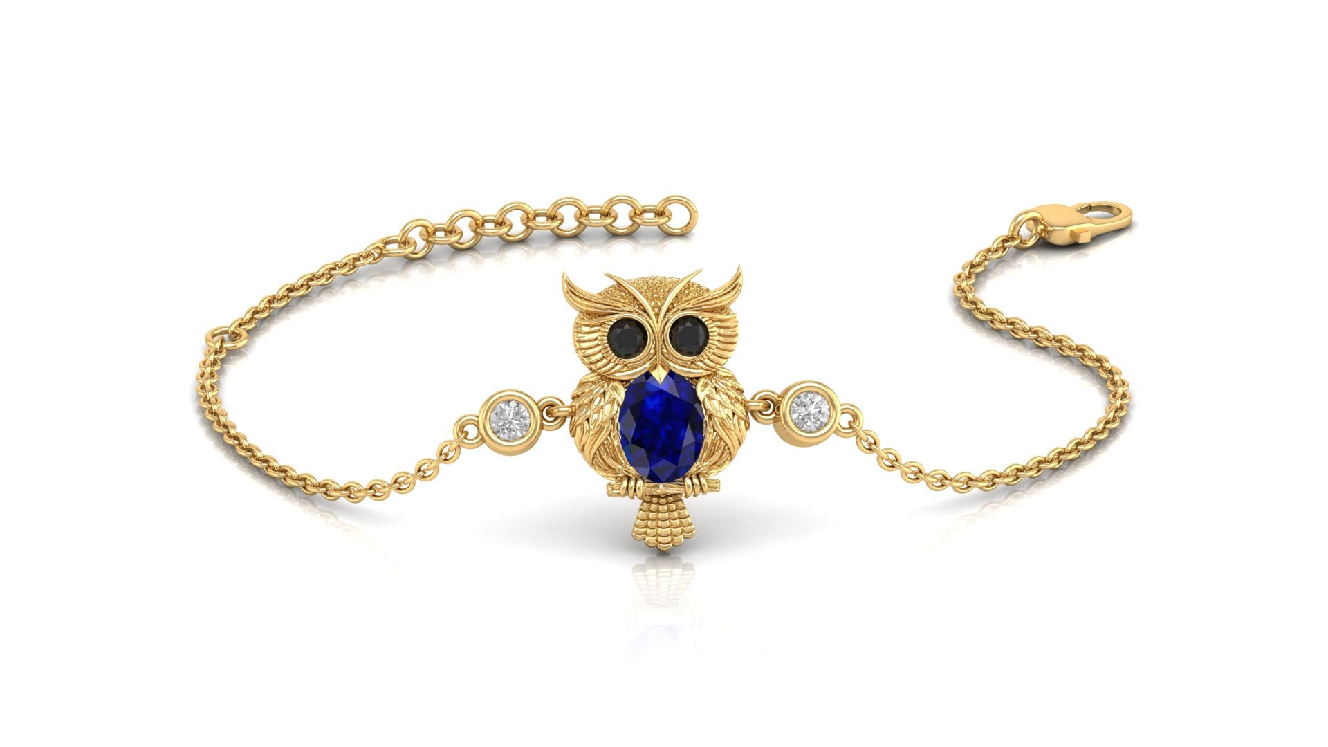 A gold chain bracelet featuring an owl pendant with a large blue sapphire gemstone center, black gemstone eyes, and small clear stones on either side, shown on a white background.