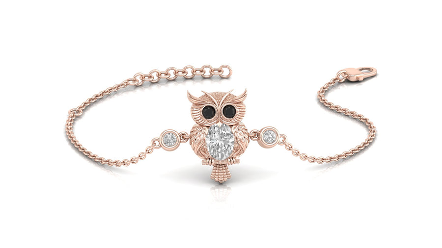 A delicate rose gold chain bracelet featuring an owl pendant with black eyes and a central clear diamond gemstone, flanked by two small clear gemstones on the chain, set against a plain white background.