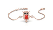A delicate rose gold chain bracelet featuring a central owl charm with a vibrant red coral gemstone, black eyes, and small clear gemstone accents, displayed on a clean white background.