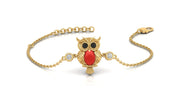 A gold chain bracelet featuring an owl pendant with a red coral for a beak, black stones for eyes, and two small clear stones on either side, shown on a white background.