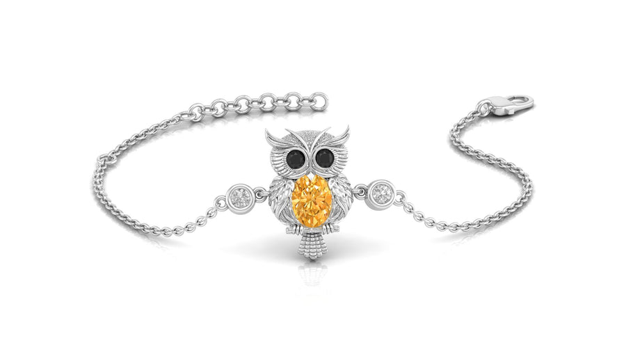 A white gold-toned chain bracelet featuring an owl pendant with a large Yellow sapphire teardrop gemstone and small clear stones, shown on a white background.