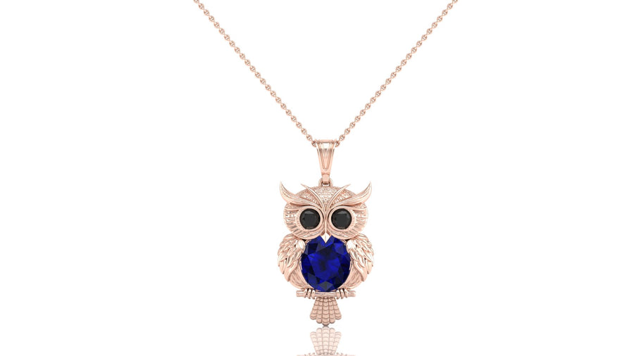 A rose gold owl pendant necklace featuring a large dark blue sapphire oval gemstone in the center, flanked by smaller dark round stones for eyes, shown on a delicate rose gold chain against a white background.