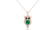 A rose gold owl pendant necklace featuring a large green emerald gemstone and small black gemstone eyes, suspended from a delicate rose gold chain against a white background.