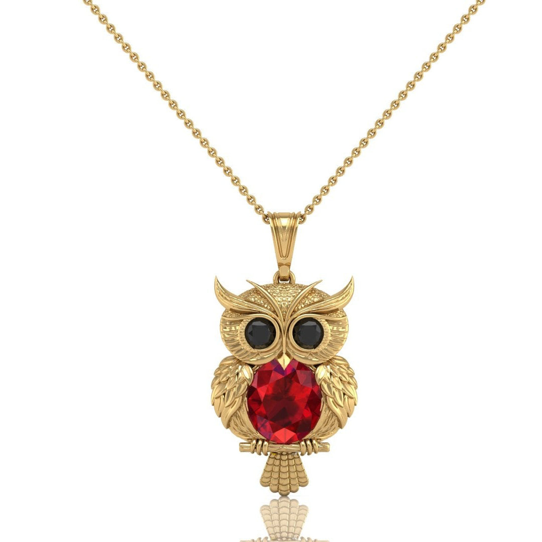 Gold owl pendant necklace featuring a large ruby gemstone and small black gemstone eyes, suspended from a delicate gold chain on a white background.