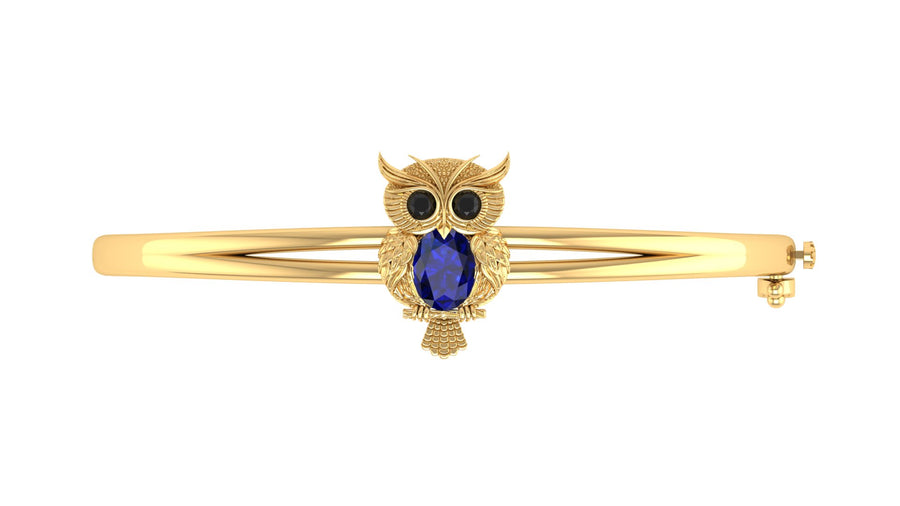 A gold bangle bracelet featuring an owl charm with black eyes and a Blue sapphire body, set against a plain white background.