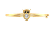 A gold bangle bracelet featuring a central owl charm with black eyes and a clear oval Diamond gemstone on its chest, set against a plain white background.