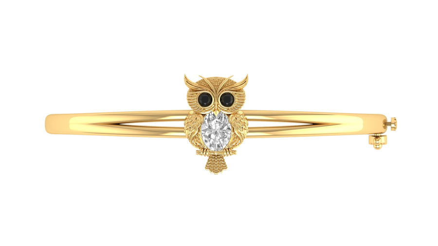 A gold bangle bracelet featuring a central owl charm with black eyes and a clear oval Diamond gemstone on its chest, set against a plain white background.