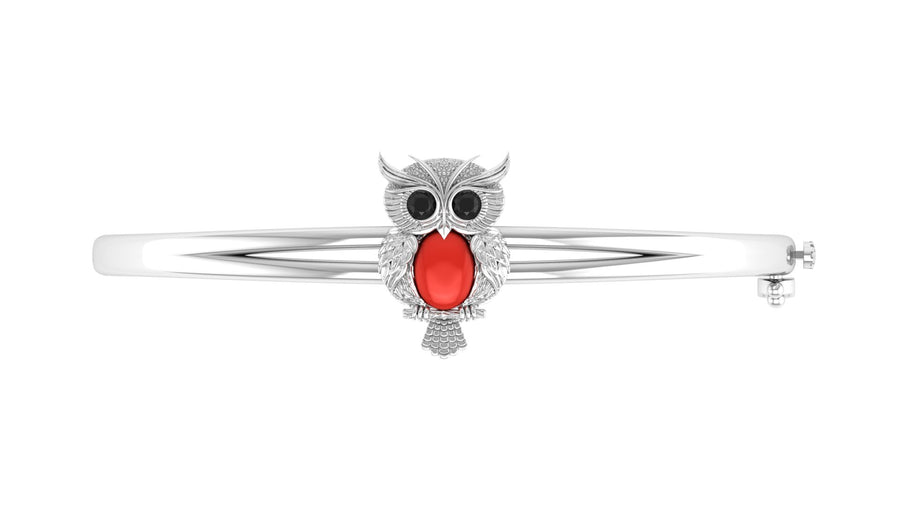 A white gold bangle bracelet featuring an owl charm with a prominent red coral centre oval stone and small clear stones, shown on a plain white background.