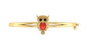 A gold bangle bracelet featuring a central owl charm with black eyes and a red coral centre stone, set against a plain white background.