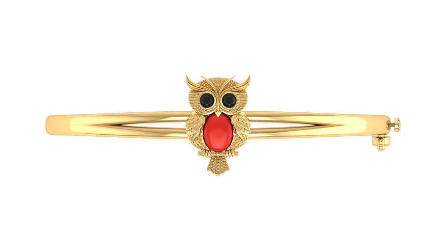 A gold bangle bracelet featuring a central owl charm with black eyes and a red coral centre stone, set against a plain white background.