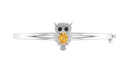 A white gold owl-shaped bangle bracelet featuring a large oval yellow sapphire gemstone in the center, flanked by small black stones for eyes and clear stones for details, set against a plain white background.