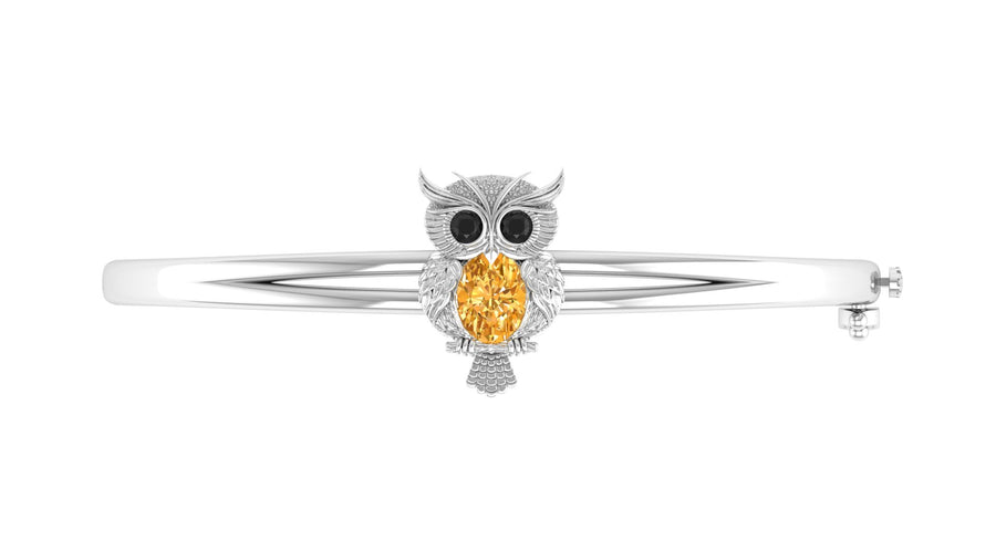 A white gold owl-shaped bangle bracelet featuring a large oval yellow sapphire gemstone in the center, flanked by small black stones for eyes and clear stones for details, set against a plain white background.