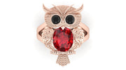 Rose gold owl-shaped brooch with a ruby gemstone on a white background