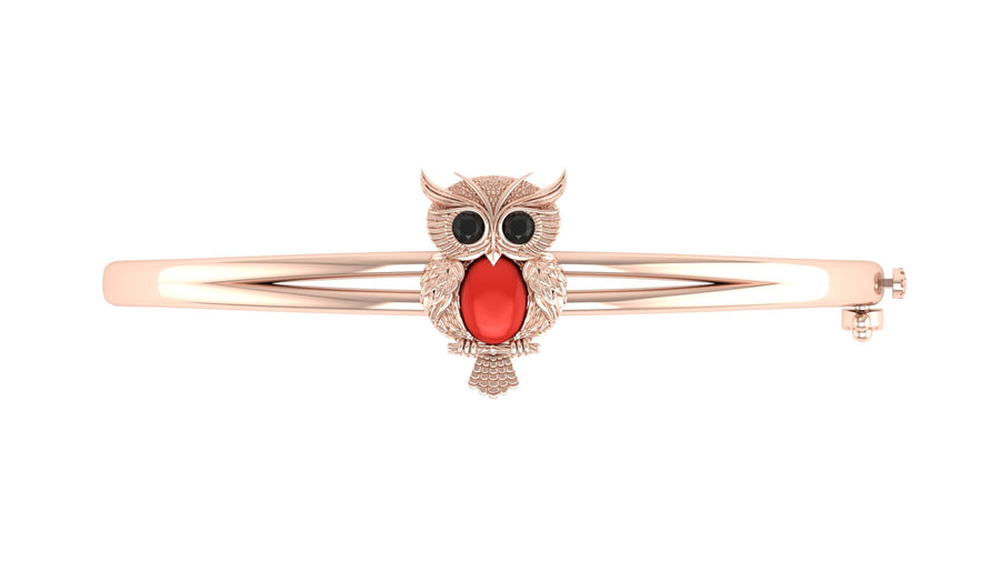 A rose gold bangle bracelet featuring a detailed owl charm with a red coral centre stone and black eyes, set against a plain white background.