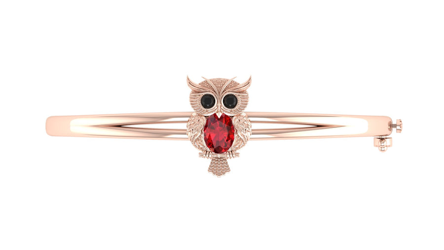 A rose gold bangle bracelet featuring an owl charm with a red ruby gemstone and black eyes, set against a plain white background.