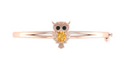 A rose gold bangle bracelet featuring an owl charm with a central yellow sapphire gemstone and small black stone eyes, set against a plain white background.